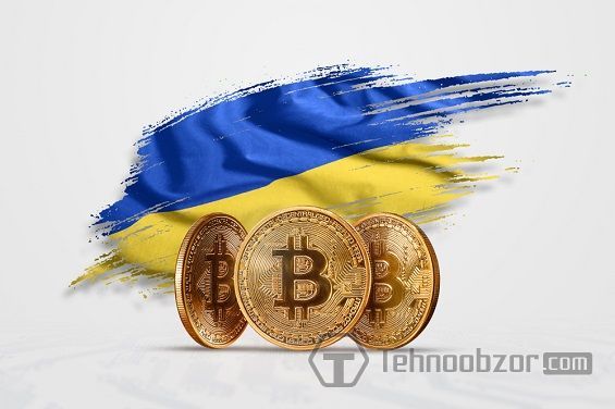 Три монетки біткоіни на тлі українського прапора